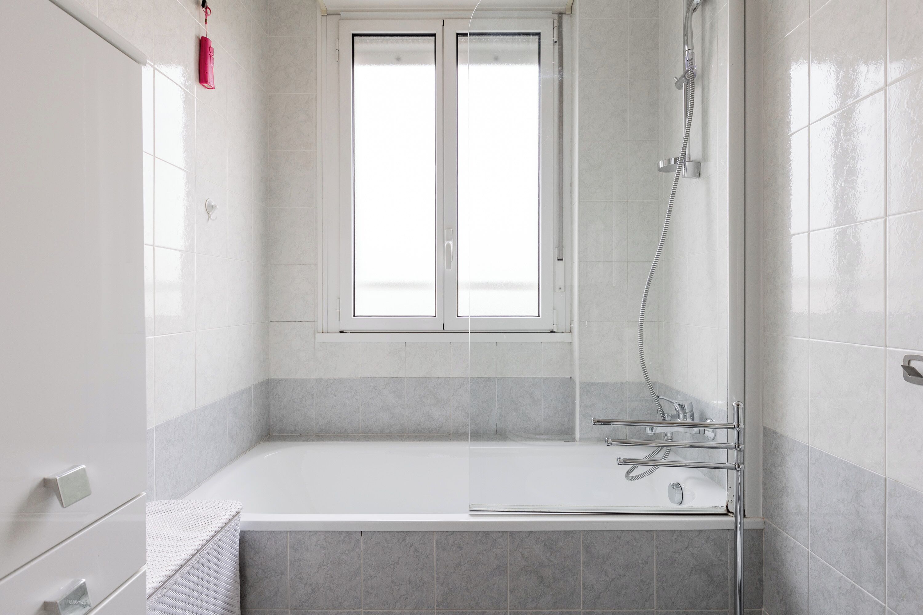 Een moderne badkamer met een bad, douche en raam.