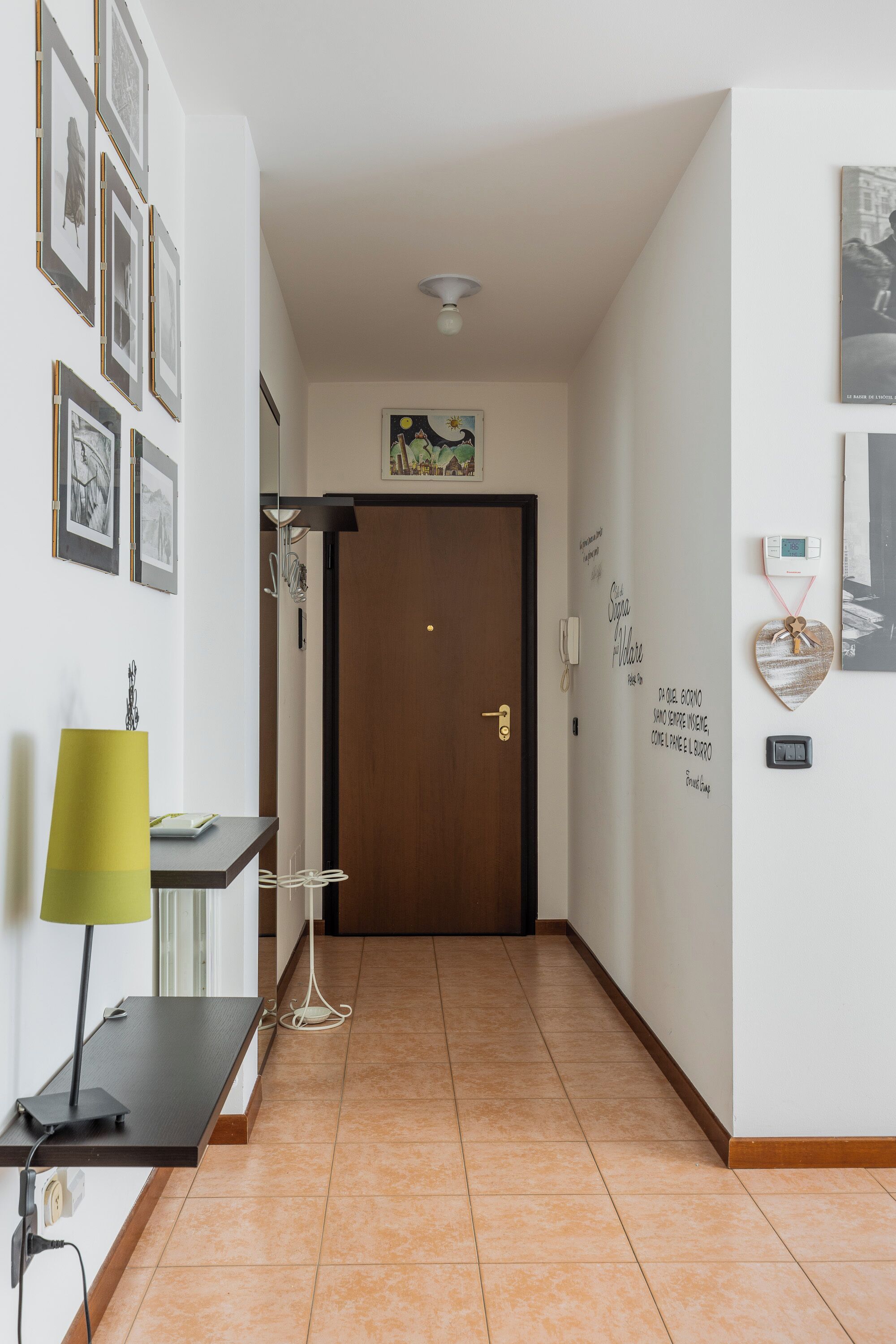 A hallway with a wooden door, a wall-mounted phone, and a heart-shaped decoration.
