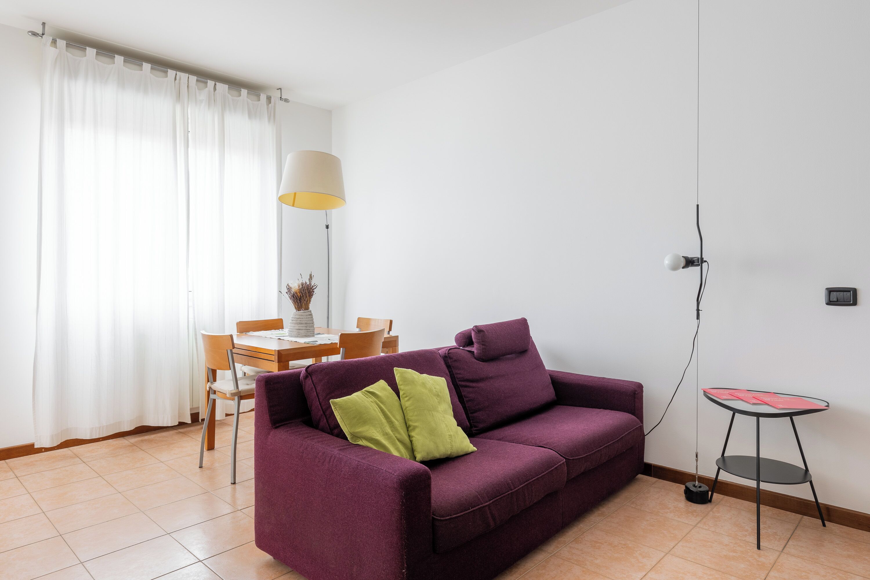 Un salon avec un canapé violet, une petite table ronde et un coin repas comprenant une table et des chaises.