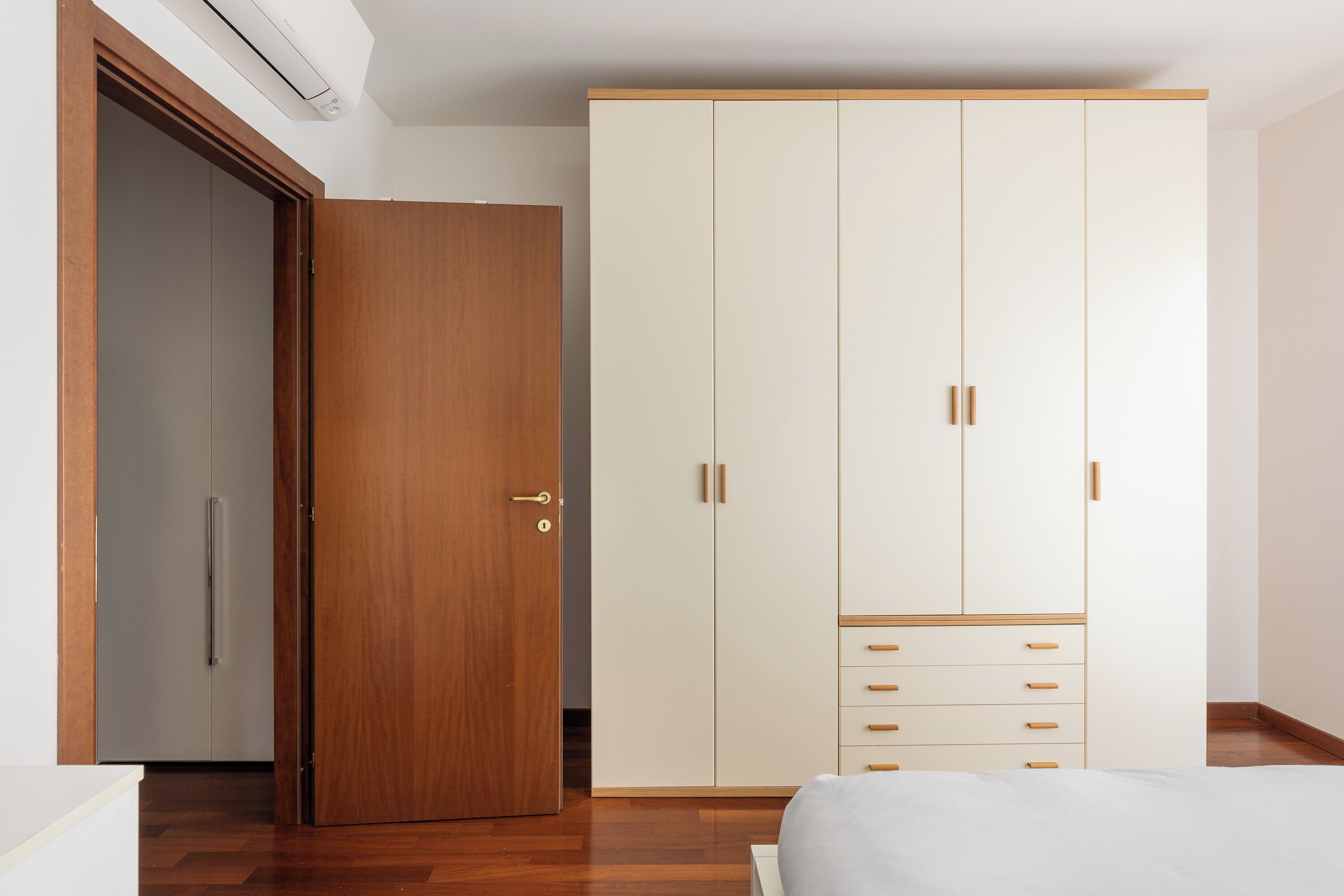 A bedroom with a wooden wardrobe, a bed, and a white bedside table.