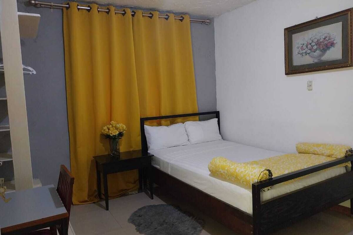 A single bed with a wooden frame, a bedside table with a vase of flowers, and a chair.