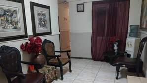 A living room with a tiled floor, two framed artworks, a vase with red flowers, and a water dispenser. - Miss. Emily Place (Monrovia)