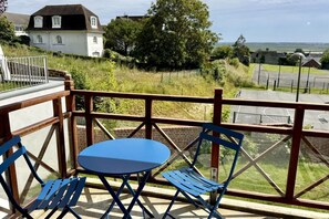 Ein Balkon mit Tisch und Stühlen, der auf eine Grünfläche mit einem Gebäude im Hintergrund blickt.