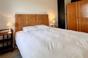 Ein Schlafzimmer mit Holz-Kopfteil, einem Bett mit weißer Bettwäsche, einem Nachttisch mit Lampe und einem Kleiderschrank.