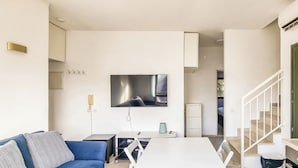 A modern living room with a flat-screen TV, a sofa, a dining table, and a kitchen area with a microwave and oven. - Ben Yehouda Obsidian (Tel Aviv)
