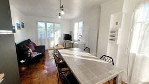A modern living room with a black sofa, a wooden dining table, and a TV. - House 4 Bdrms and Terrace, Garden near. Sea, Golfs, Salt marshes, Walks (Guérande)