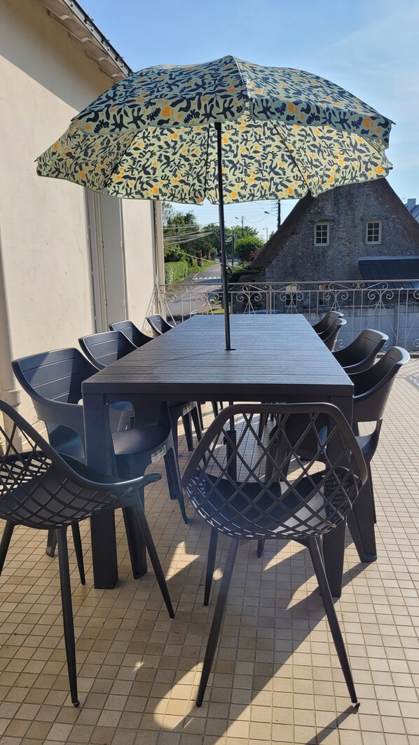 An outdoor dining area with a table and chairs, an umbrella, and a stone building in the background.