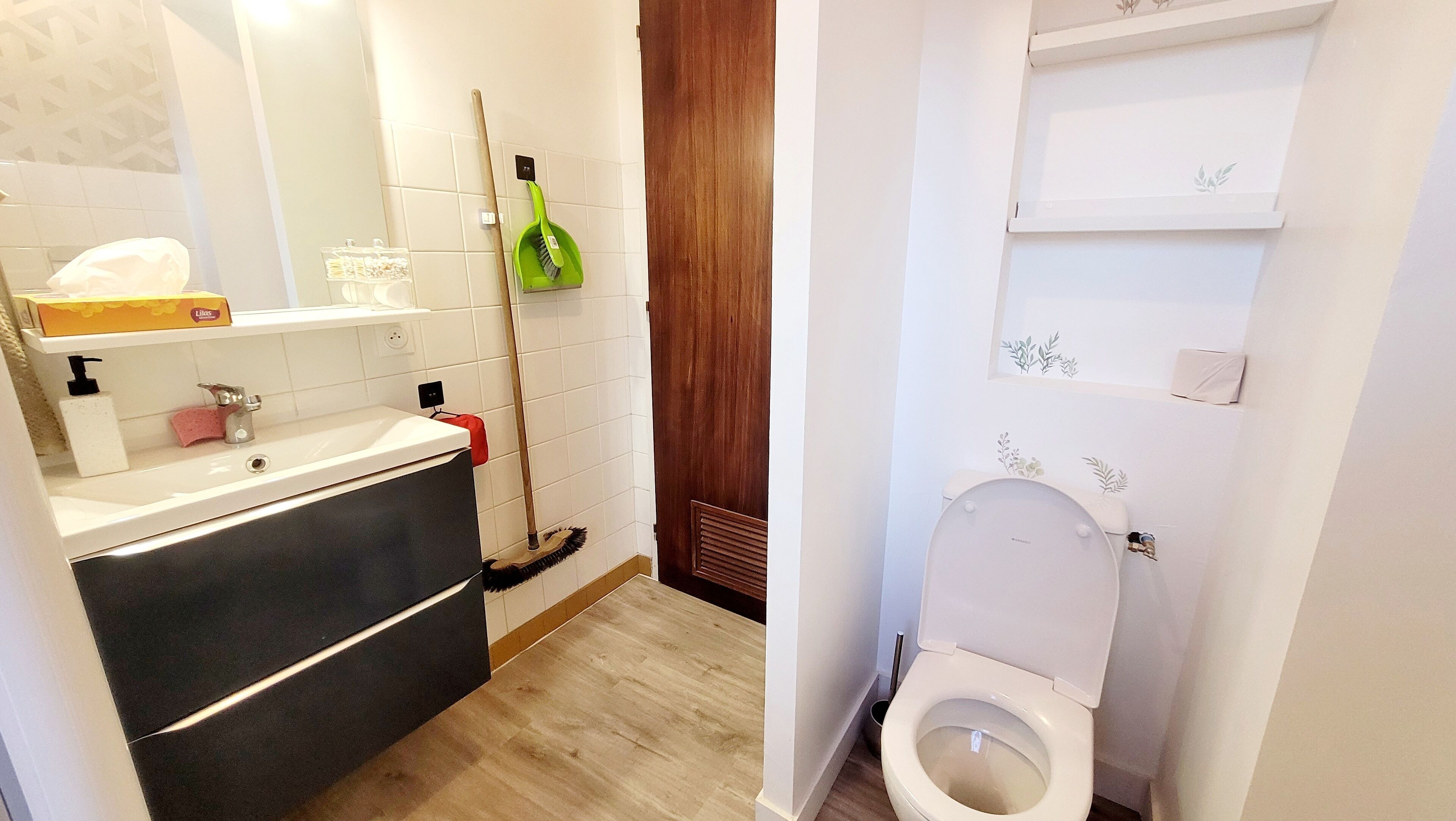Ein Badezimmer mit Waschbecken, Toilette und einem Mopp, der an der Wand lehnt.