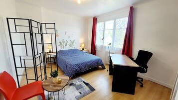 Una camera compatta con un letto, una scrivania, una sedia e un tavolino con una pianta.