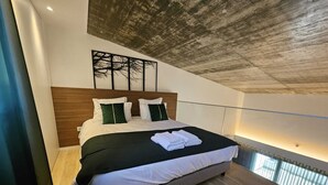 A modern bedroom with a large bed, a wooden headboard, and a view of the sky through a skylight. - Marinha Grande Apartament GREEN LOFT N°6 (Marinha Grande)
