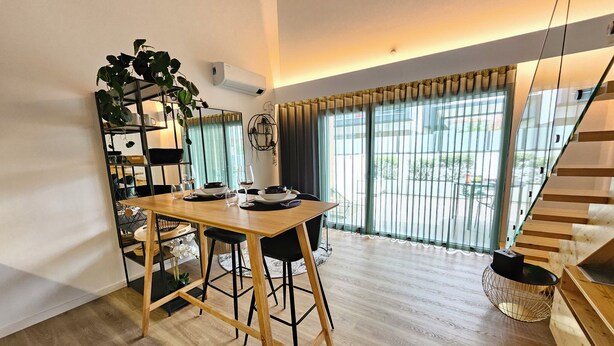 A dining area with a wooden table, chairs, and a plant. There is a staircase with a wooden railing and a hanging basket. - Marinha Grande Apartament GREEN LOFT N°6 (Marinha Grande)