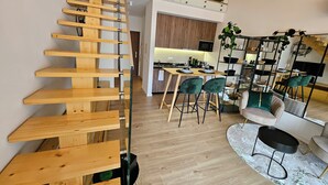A modern interior with a wooden staircase, a dining area with green chairs, and a kitchen in the background. - Marinha Grande Apartament GREEN LOFT N°6 (Marinha Grande)