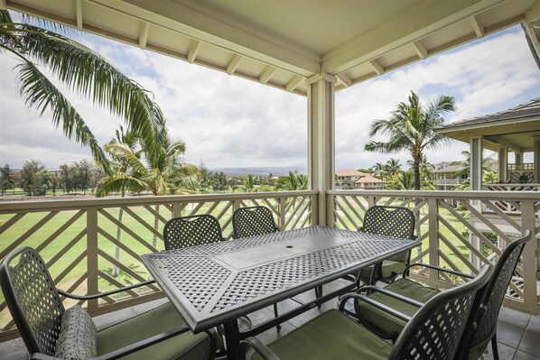 A covered outdoor seating area with a table and chairs, overlooking a landscaped garden and distant hills.