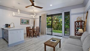 A modern living room with a sofa, a wooden coffee table, a dining area with chairs, a kitchen island, and a ceiling fan.