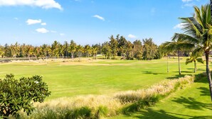 Un campo de golf con cielo despejado, palmeras y un césped bien cuidado.
