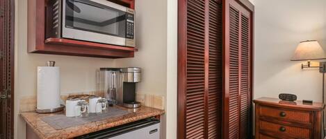 Eine kompakte Küche mit Mikrowelle, Kaffeemaschine und Toaster, einem Kühlschrank und einem Holzschrank.