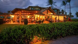 An outdoor restaurant with multiple dining areas, palm trees, and a view of the ocean.