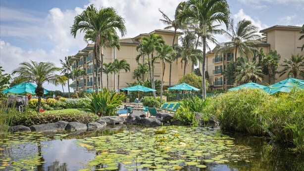 A resort with a pool surrounded by palm trees and a building with balconies.