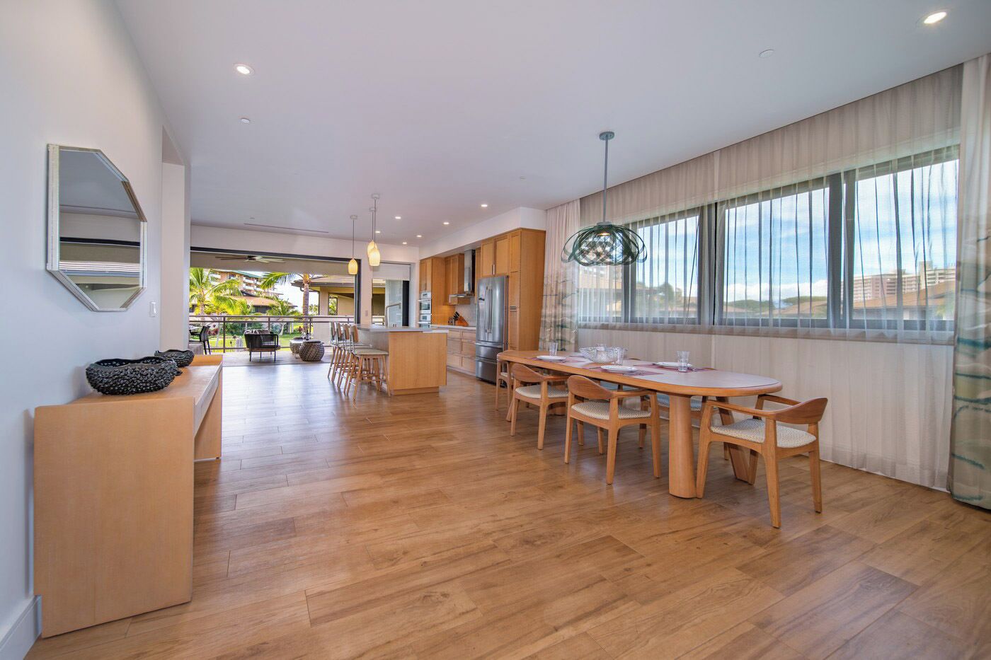 Una cocina amplia con suelo de madera, una zona de comedor con una mesa redonda y sillas, y ventanas grandes con cortinas.