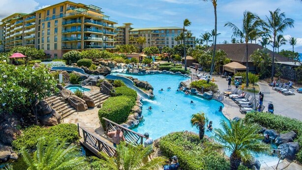 A resort with a large pool area, palm trees, and a multi-story building with balconies.