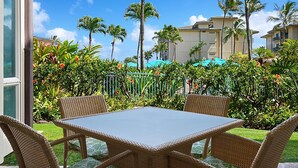 Een terras met rieten meubilair en een glazen tafel, omgeven door weelderige begroeiing en palmbomen.