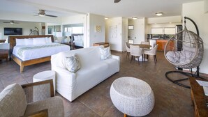 A spacious hotel room with a large bed, a sofa, a dining area, and a kitchen.