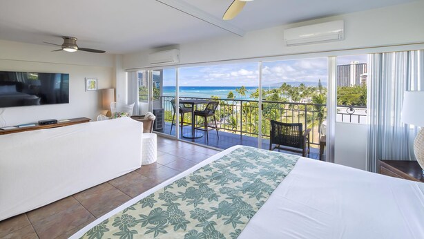 A hotel room with a balcony, a bed, a desk, and a TV.
