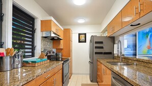 Une cuisine moderne dotée de plans de travail en granit, d’appareils électroménagers en acier inoxydable, d’armoires en bois et d’une fenêtre avec des stores.
