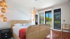 Une chambre à coucher avec un lit, des tables de chevet, un ventilateur de plafond et une vue sur l’extérieur, accessible par une porte coulissante.