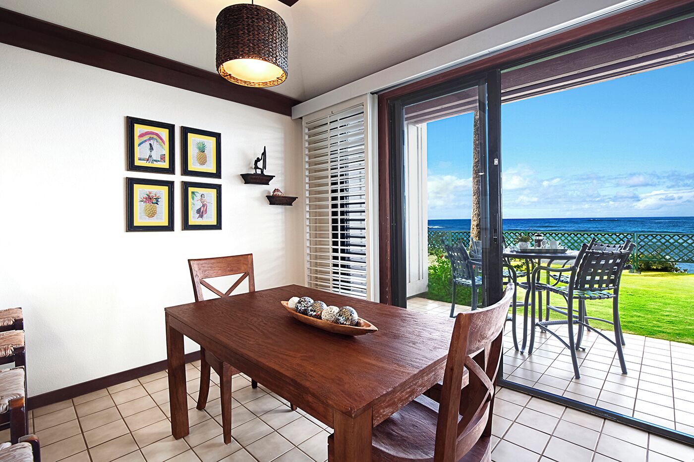 A dining area with a wooden table and chairs, a decorative bowl, and a view of the ocean through a sliding glass door.