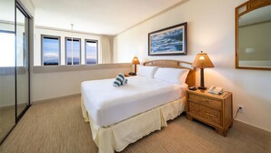 A hotel room with a large bed, a bedside table with a lamp, a nightstand with a phone, a window with a view of the sea, and a painting on the wall.