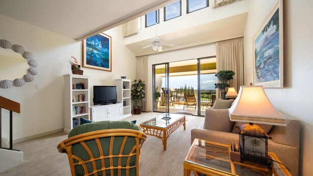 A spacious living room with a television, bookshelves, a sofa, and a balcony with a view.