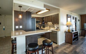 A modern kitchen with a central island, bar stools, a built-in oven, and a microwave.