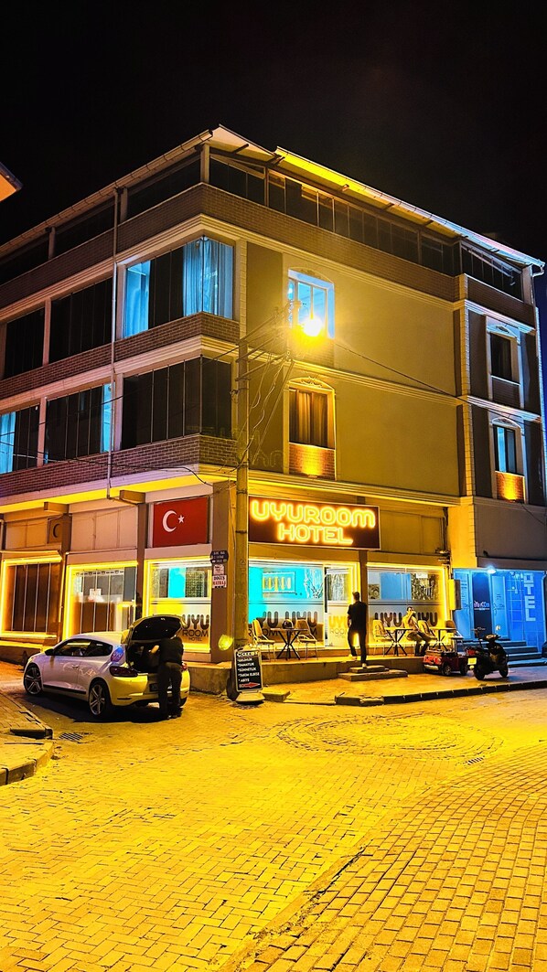 A hotel with a prominent sign, a car parked in front, and a paved area in front.