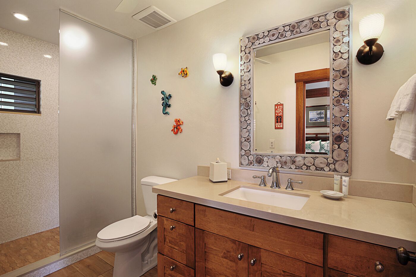 Une salle de bain comprenant des toilettes, un lavabo, un miroir avec un cadre décoratif, des meubles en bois et des luminaires fixés au mur.