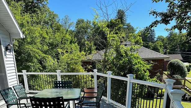 Une terrasse en bois avec une table et des chaises, entourée d’une balustrade blanche.