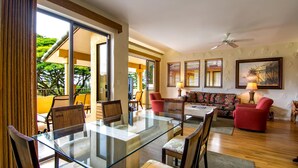 A spacious living area with a glass-top dining table, comfortable seating, and a view of the outdoors.