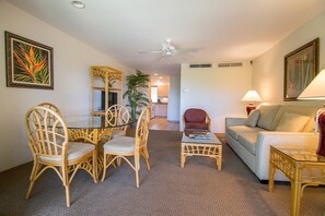 A living room with a dining table, chairs, a sofa, a coffee table, and a ceiling fan.
