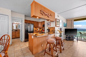 A modern kitchen with a central island, wooden cabinets, and a large TV on a balcony.