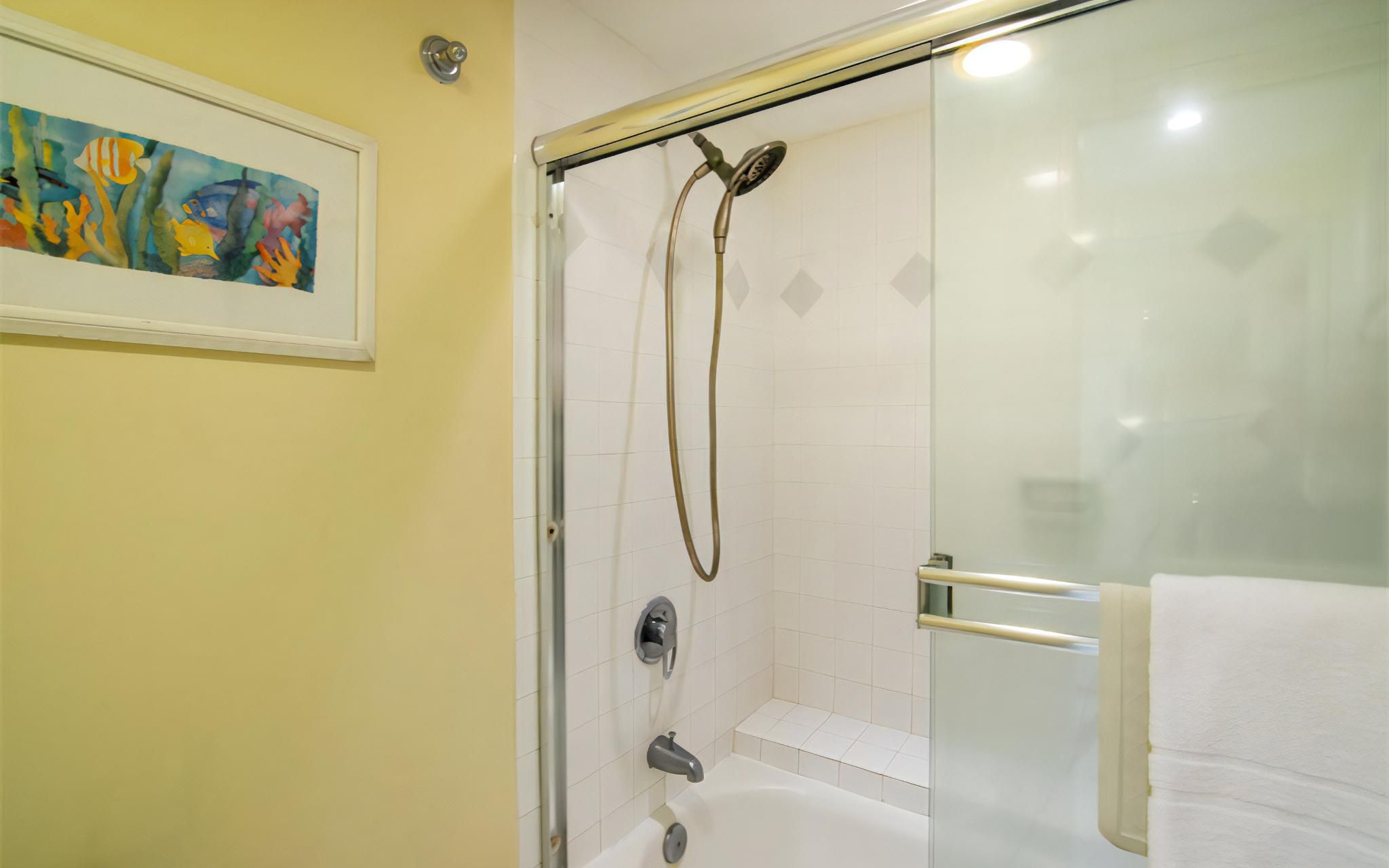 Ein Badezimmer mit Duschabtrennung aus Glas, einer Badewanne und einem gerahmten Bild an der Wand.