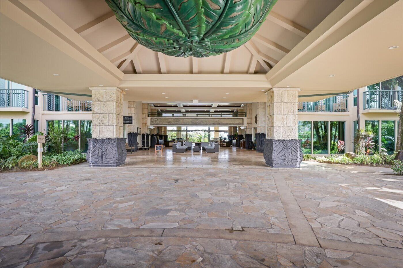 Un'ampia hall con pavimento in pietra, grandi colonne e un'ornamentale decorazione a forma di foglia verde.