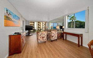 A spacious living area with a flat-screen TV, wooden furniture, and large windows offering a view of the outdoors.