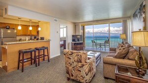 A hotel room with a kitchen, bar area, a sofa, and a view of the ocean.