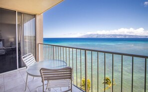 Ein Balkon mit Tisch und Stühlen mit Blick auf das klare, blaue Meer und entfernte Berge.