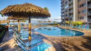 A poolside area with lounge chairs, a thatched umbrella, and a building with balconies.