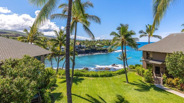 Un resort con vistas al océano, palmeras y un césped bien cuidado.
