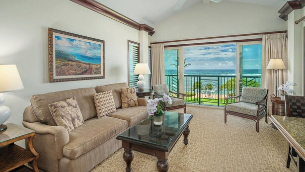 A room with a sofa, a coffee table, and a chair. There is a large window with a view of the ocean.