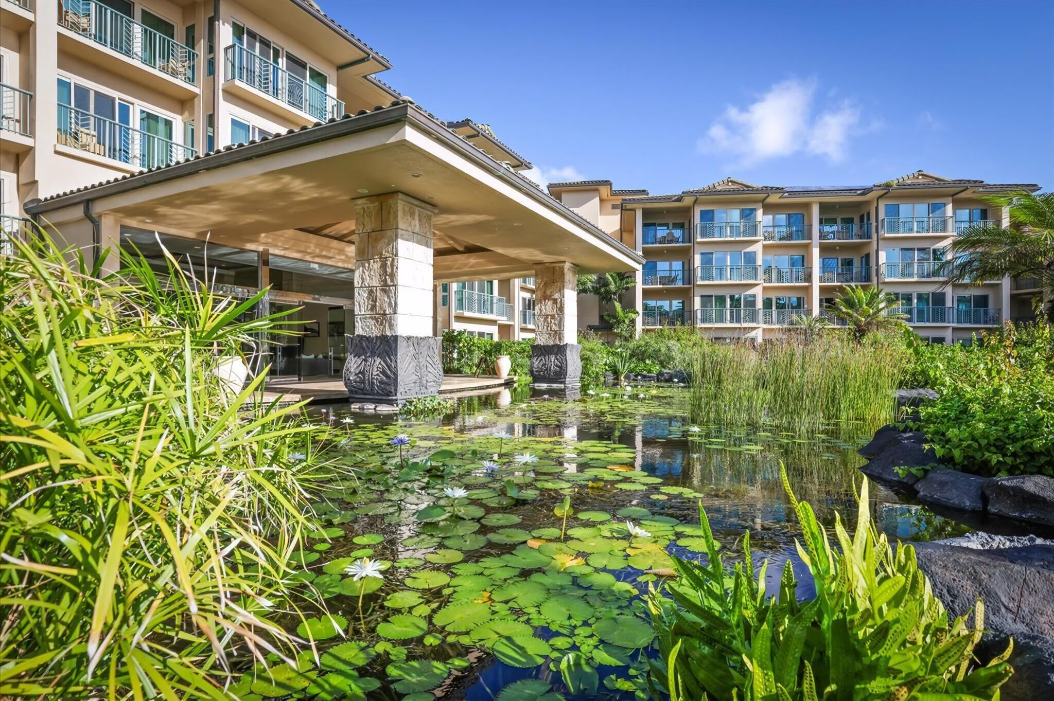 Een hotel met een overdekt buitengebied, een vijver met waterlelies en een gebouw met meerdere balkons.