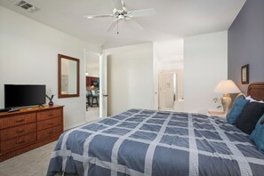 Ein Schlafzimmer mit Bett, Kommode, Fernseher und Deckenventilator.