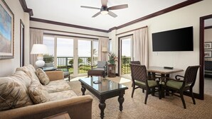 Habitación de hotel con balcón, ventilador de techo, televisor de pantalla plana, mesa de comedor con sillas y sofá.